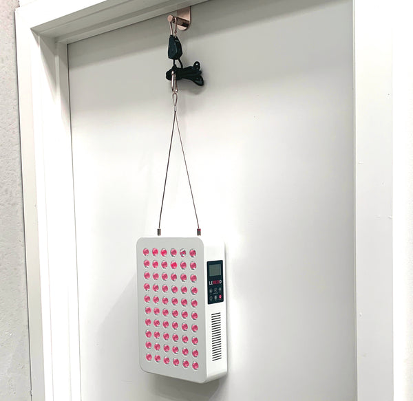 White electronic device with pink lights hanging from a hook on a white wall.