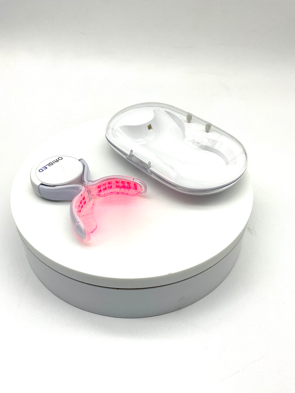 ORISLED intraoral red light therapy device with LED mouthpiece illuminated, resting in open white charging sterilisation case