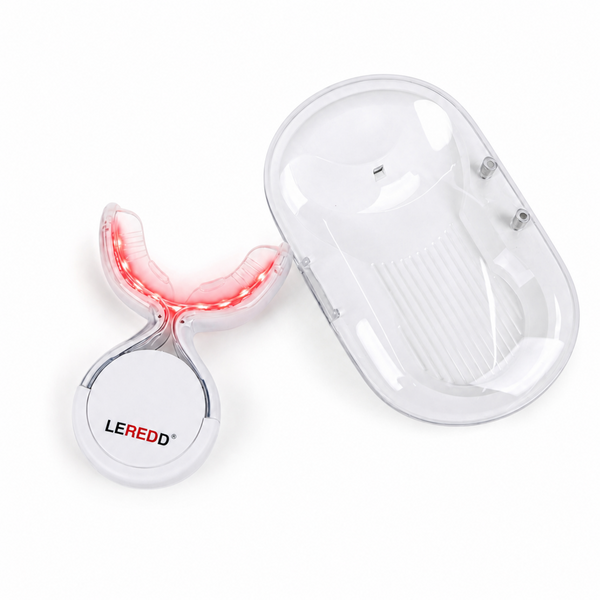 A white LED light therapy device with a clear protective cover and a matching oval charging case, shown on a clean white background. The device is illuminated with a red light, and the brand name 'LEREDD' is visible on the circular base.