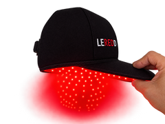 A black LED light therapy cap with the brand name 'LEREDD' embroidered on the side, held by a hand to demonstrate the red light therapy glow emanating from the underside.