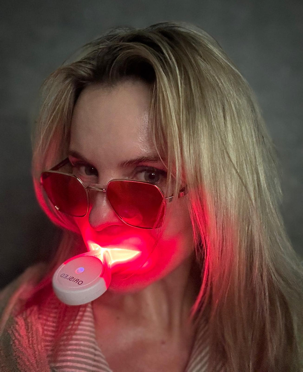 A white LED light therapy device with a clear protective cover and a matching oval charging case, shown on a clean white background. The device is illuminated with a red light, and the brand name 'LEREDD' is visible on the circular base.
